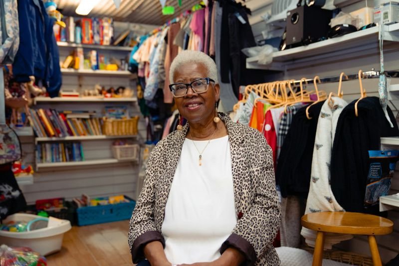 A smiling shop owner sitting in her store among racks of clothing