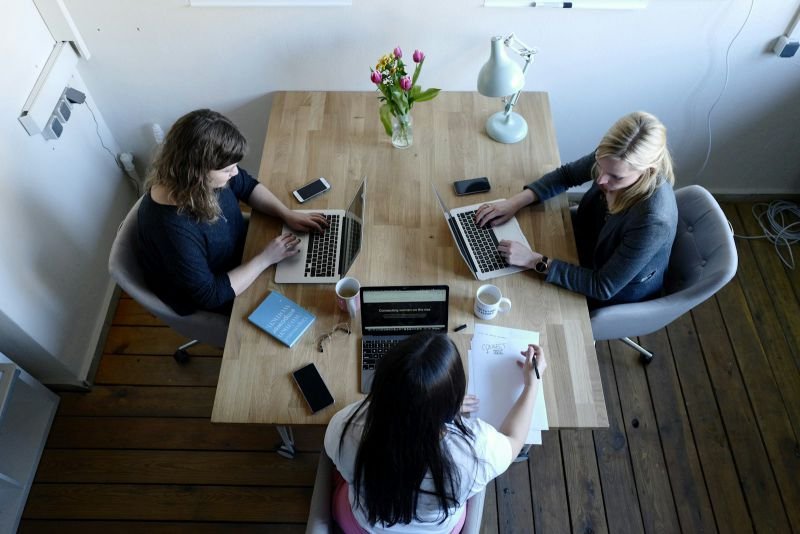 Overhead view of three colleagues working on laptops around a wooden table