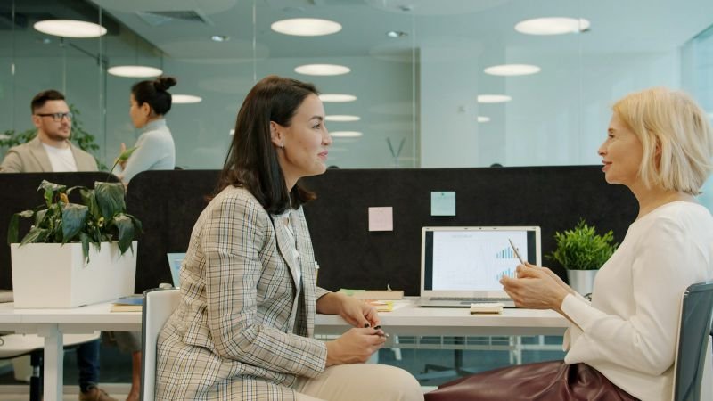 Two colleagues talking through a plan at a shared desk in an open office