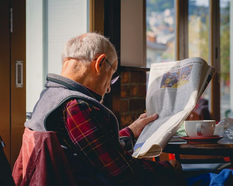 An older man reading the newspaper over a cup of coffee