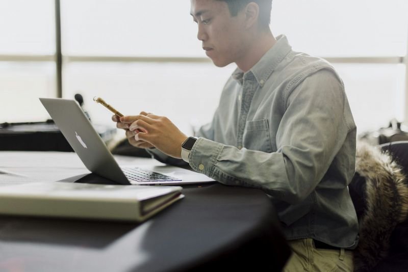 A man checking his phone while he works on a laptop at his desk