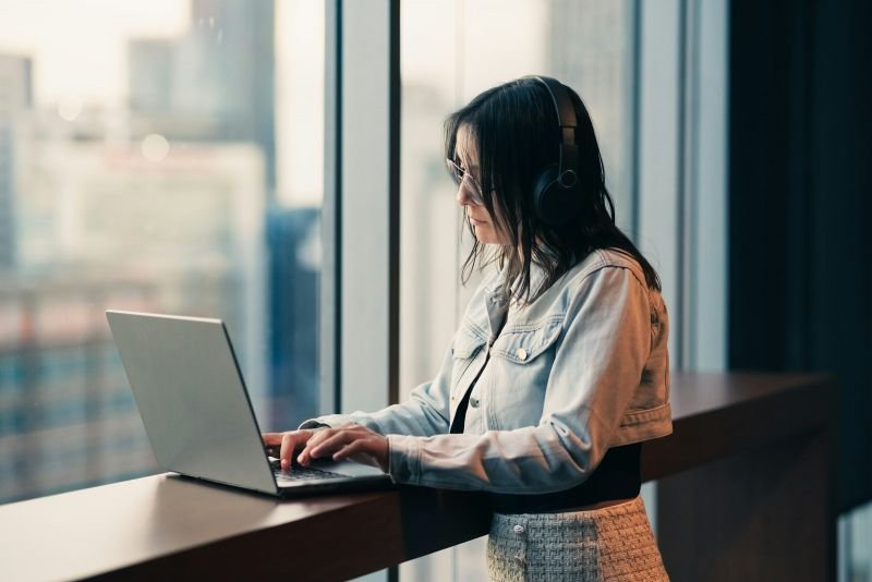 A professional working on her laptop at a standing desk beside a large window