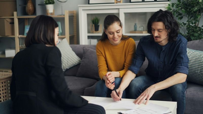 A couple signing home financing paperwork with an adviser in their living room