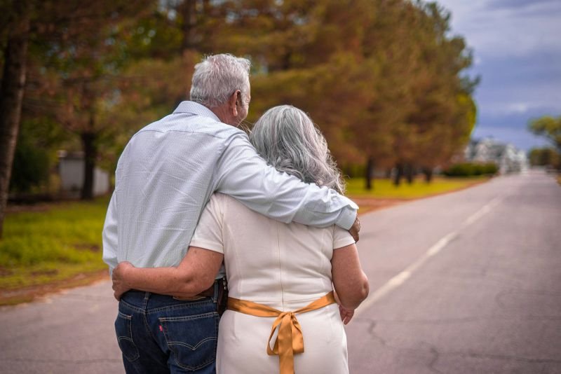An older couple walking arm in arm along a quiet tree-lined road
