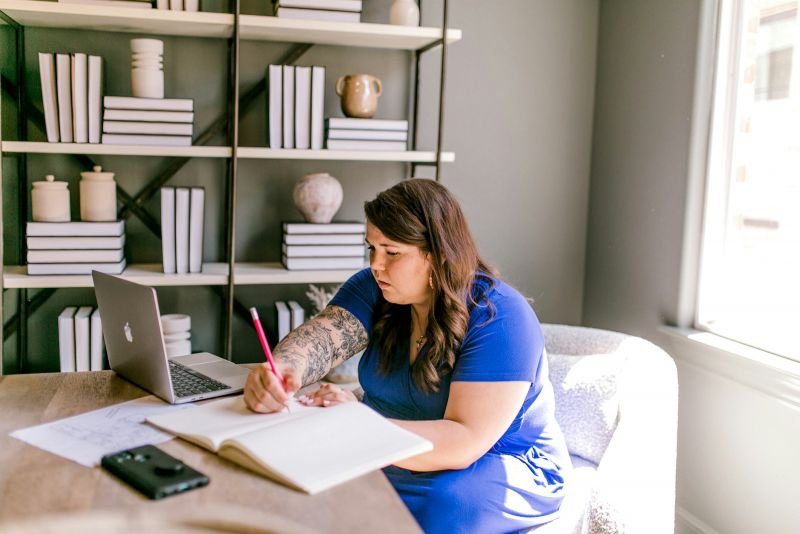 A woman writing in a notebook beside her laptop as she plans her savings goals at home